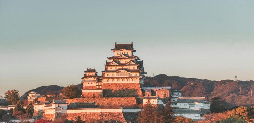 Scenic view of Himeji Castle surrounded by vibrant autumn foliage during sunset.